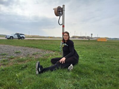 Tina Kronberg sitter fastkedjad vid en stolpe på flygplatsens landningsbaneområde.