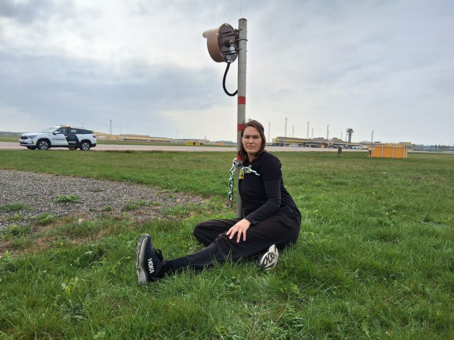 Tina Kronberg sitter fastkedjad vid en stolpe på flygplatsens landningsbaneområde.