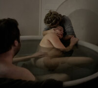 En man och en födande kvinna i ett badkar. En barnmorska kramar kvinnan.