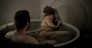 En man och en födande kvinna i ett badkar. En barnmorska kramar kvinnan.