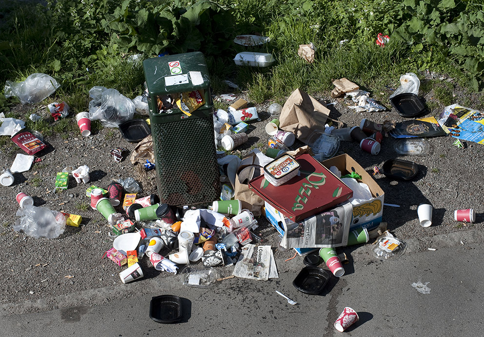 Engångsmuggar och matförpackningar ligger utspridda kring en överfull papperskorg – ett exempel på den höga användningen av engångsprodukter i Sverige.