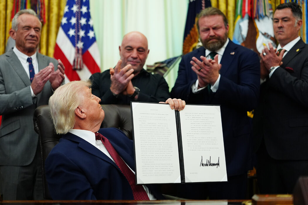 Trump håller upp ett dokument för en grupp män som ser nöjda ut