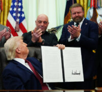 Trump håller upp ett dokument för en grupp män som ser nöjda ut