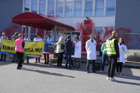 Forskare med banderoller utanför rödmålad privatjetterminal på Bromma flygplats.