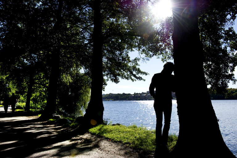 kvinna står lutad mot träd vid vatten