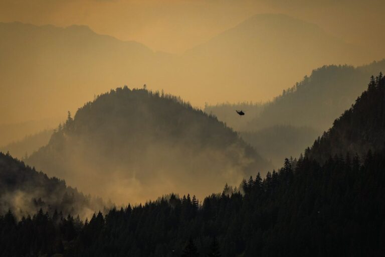 Brandrök stiger över en skog i Kanada. En helikopter syns också på bilden.