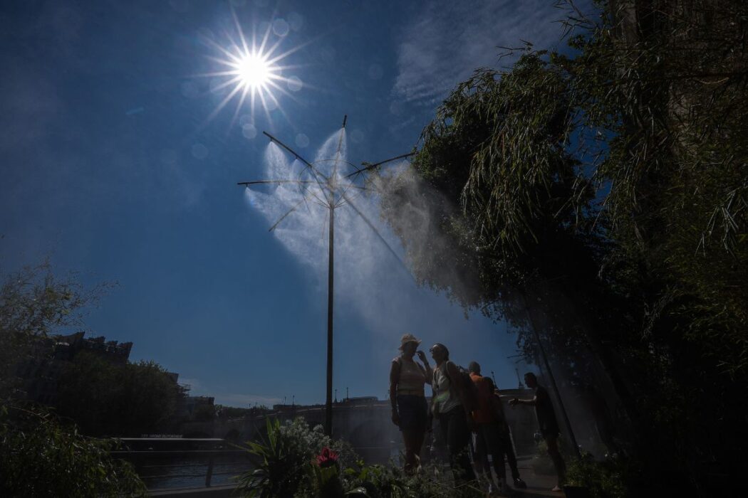 Människor svalkar sig under dimspridare i Paris under en värmebölja, lördagen den 11 juli 2026.
