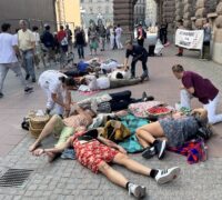 Aktivister spelar sjuka eller döda på marken, medan sjukvårdspersonal tittar till dem.