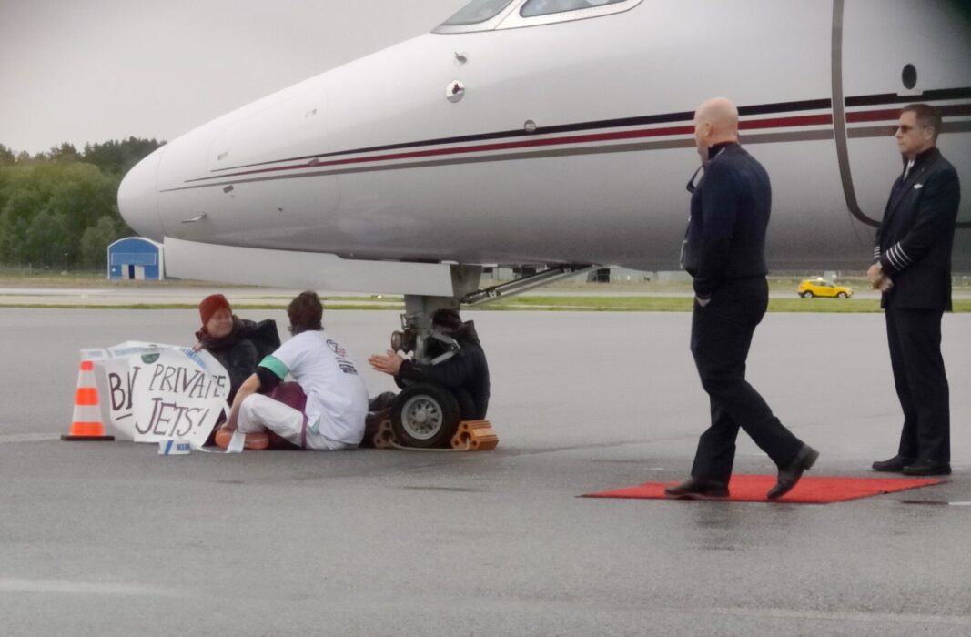 Tre aktivister sitter under nosen av ett flygplan.