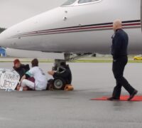Tre aktivister sitter under nosen av ett flygplan.