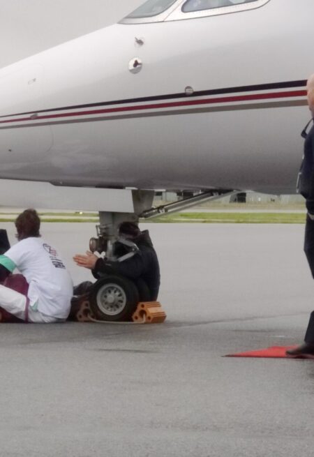 Tre aktivister sitter under nosen av ett flygplan.