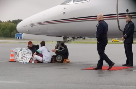 Tre aktivister sitter under nosen av ett flygplan.
