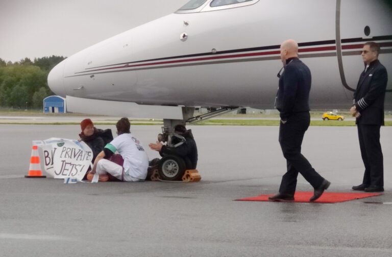 Tre aktivister sitter under nosen av ett flygplan.