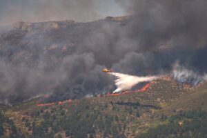 Ett flygplan arbetar med släckningsarbete över en skogsbrand.