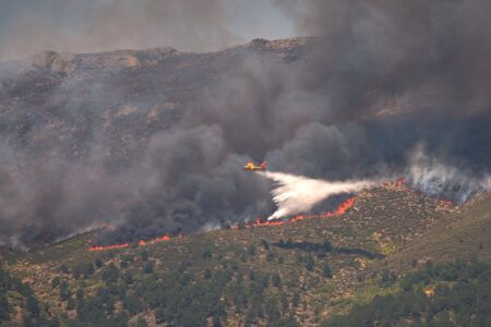 Ett flygplan arbetar med släckningsarbete över en skogsbrand.