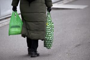 En kvinna med grön tygkasse och grön plastpåse i var hand.