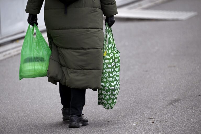 En kvinna med grön tygkasse och grön plastpåse i var hand.